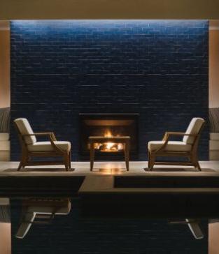 Two modern white chairs face each other in front of a fireplace and a dark blue brick wall.